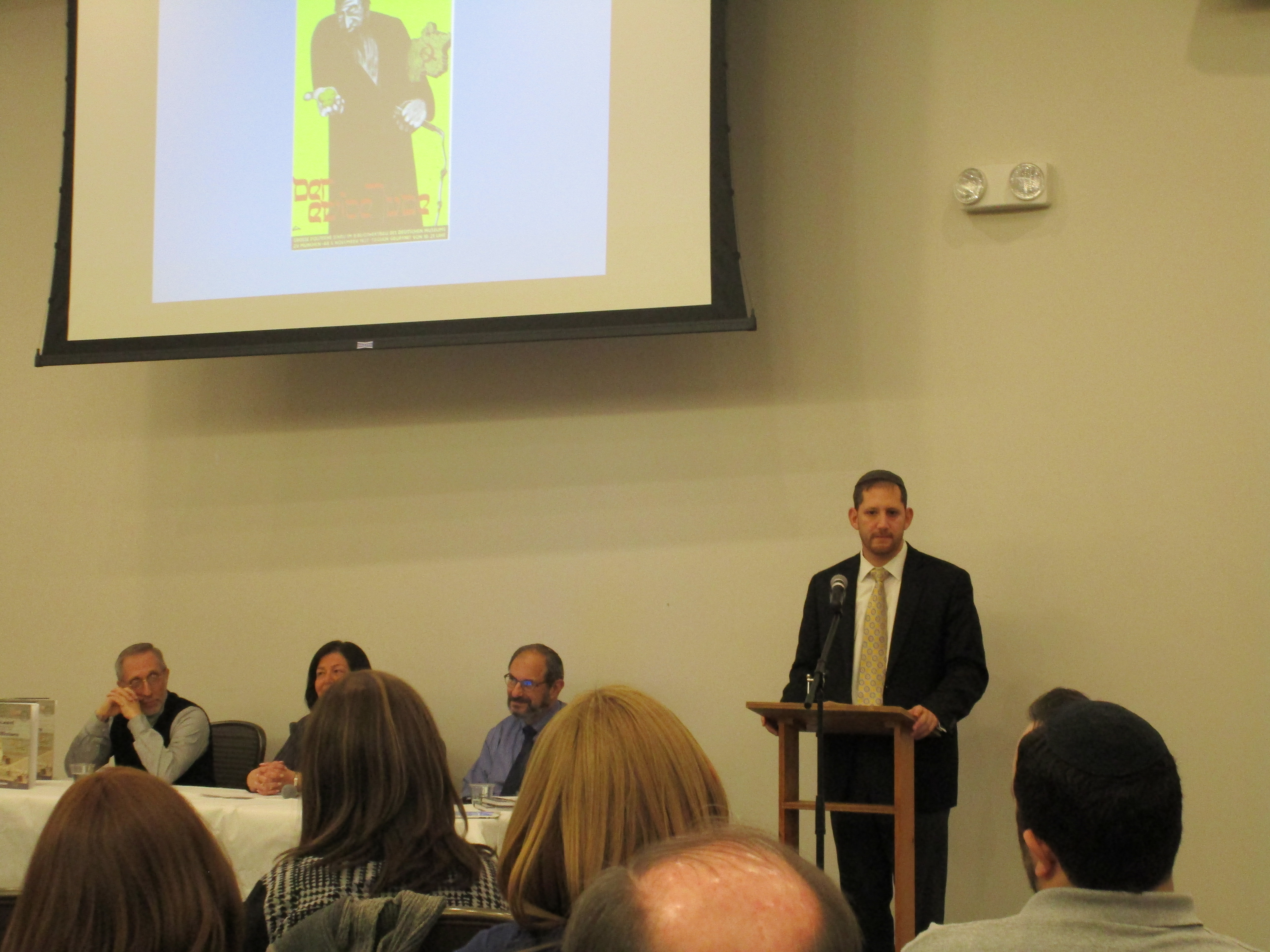 Howard Weiss, Regine Schlesinger, and Justin Gordon listen as Rabbi Shaanan Gelman delivers his remarks on the horrors of the Holocaust. 